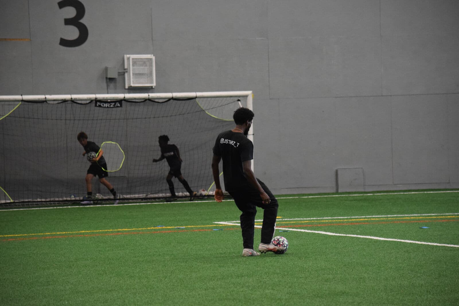A JStarz coach setting up a technical drill while players train behind.