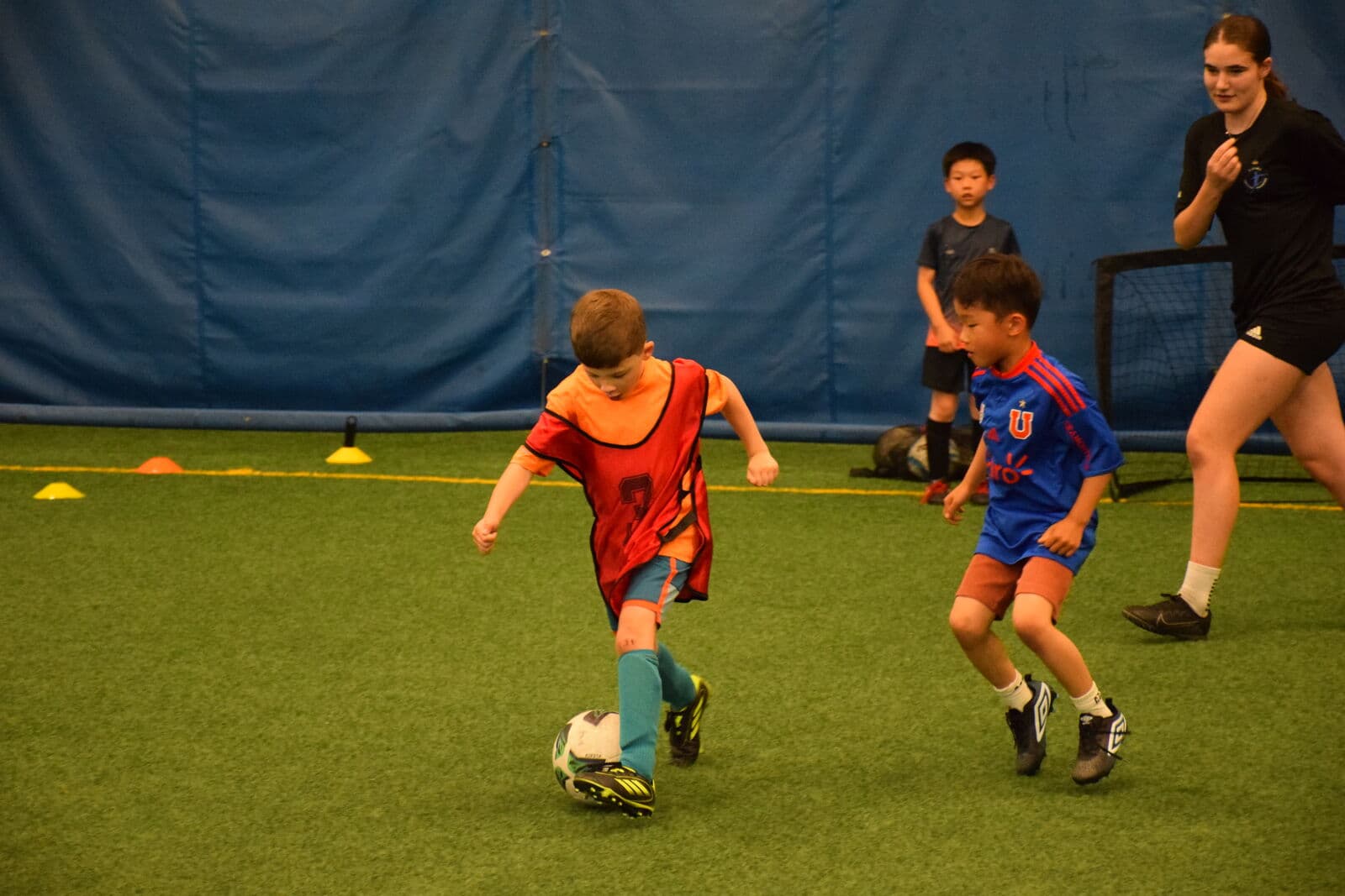 A JStarz coach guiding a young player through a cone drill in the gym.